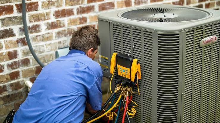 HVAC technician servicing a residential outdoor air conditioning condenser with diagnostic gauges